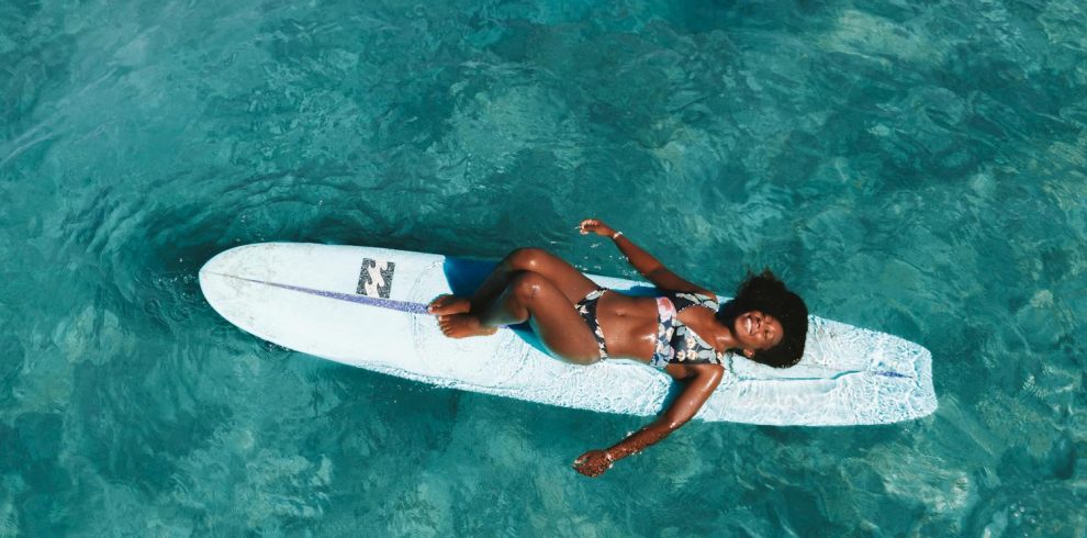 A woman in a bikini lying on a surfboard in clear blue water, enjoying a sunny day.