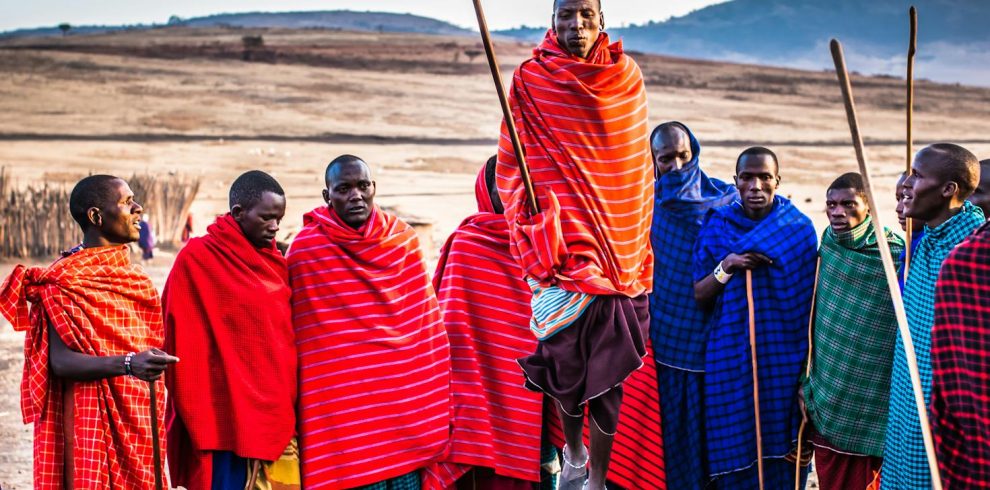 A group of Maasai men in vibrant traditional attire performing a cultural jumping dance outdoors.